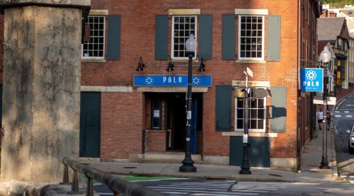 A brick building with blue signage reading "PALO," featuring large windows and a streetlamp outside.