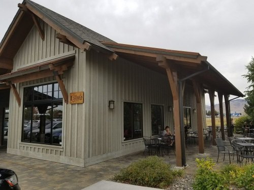 A modern building with a wooden facade, featuring outdoor seating and large windows, set in a scenic area.