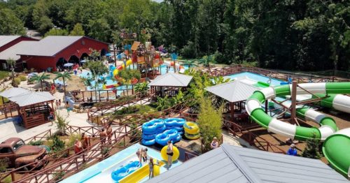 Aerial view of a water park featuring slides, pools, and colorful attractions surrounded by trees.