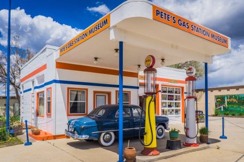 A vintage gas station museum with a classic car parked outside, featuring retro gas pumps and colorful signage.