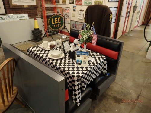 A diner booth with a checkered tablecloth, set with dishes, a small flag, and a decorative centerpiece.