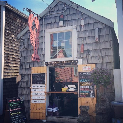 A rustic seafood shop with a wooden exterior, featuring a lobster sign and menus for fresh fish and lobster dishes.