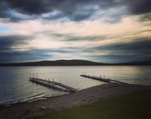 A serene lakeside view with two wooden docks extending into calm waters under a cloudy sky.
