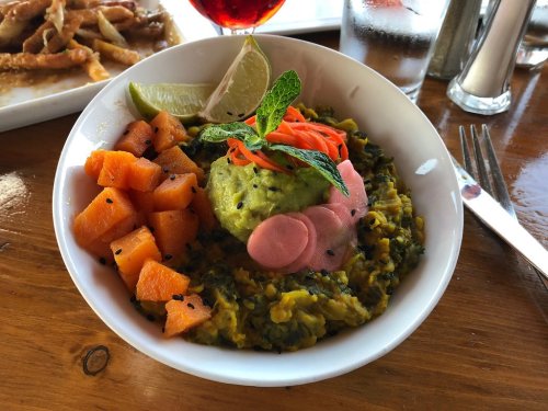 A bowl of green mash topped with pickled vegetables, garnished with mint and served with diced orange squash on the side.