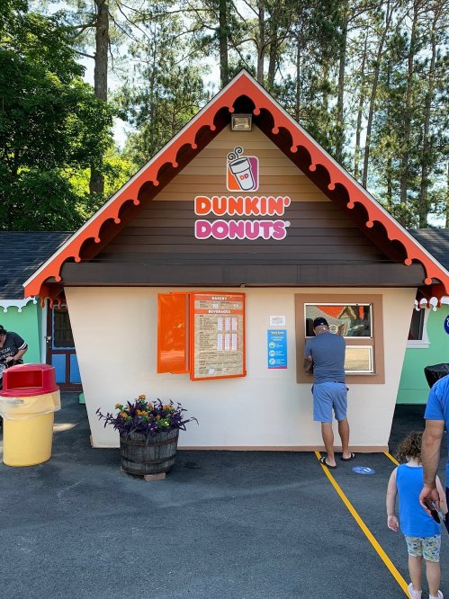 A small Dunkin' Donuts stand with a colorful exterior, featuring a menu board and a customer ordering at the window.
