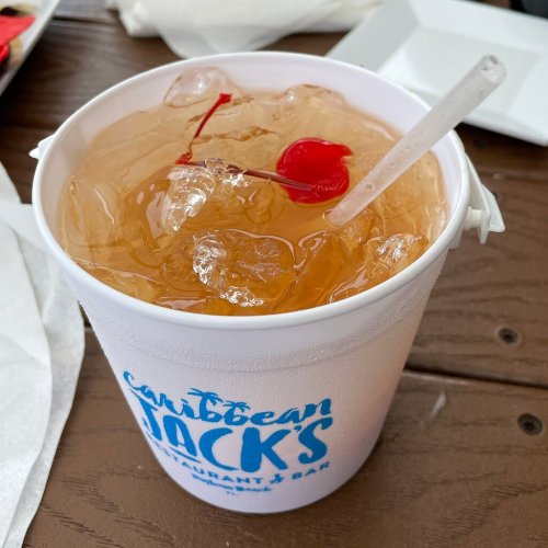 A refreshing drink with ice and cherries served in a white cup from Caribbean Jack's restaurant.