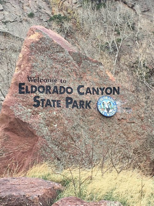 Sign welcoming visitors to Eldorado Canyon State Park, featuring a large rock and a colorful park emblem.