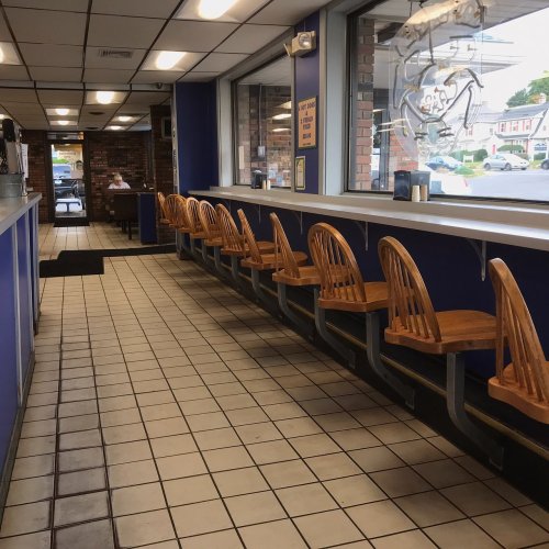 Interior of a casual dining restaurant featuring a row of wooden chairs along a counter and tiled floor.