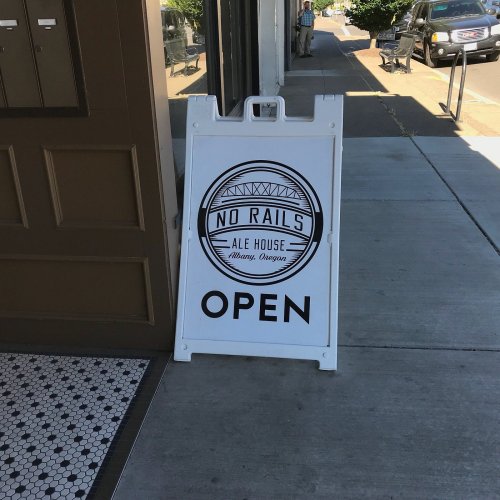 A sidewalk sign for No Rails Ale House in Albany, Oregon, displaying "OPEN" in bold letters.