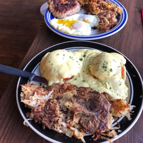 A plate of eggs Benedict with hash browns, alongside a plate with a burger and two fried eggs.