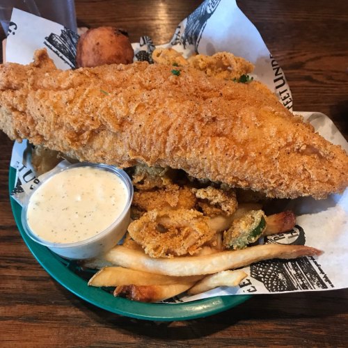 A plate of fried fish with a side of fried shrimp, fries, and a small cup of dipping sauce.
