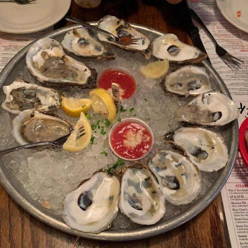A platter of fresh oysters on ice, garnished with lemon wedges and cocktail sauce.