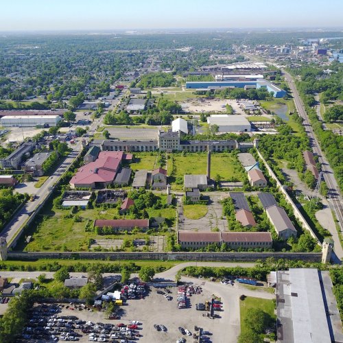 Aerial view of an abandoned industrial complex surrounded by greenery and urban development.