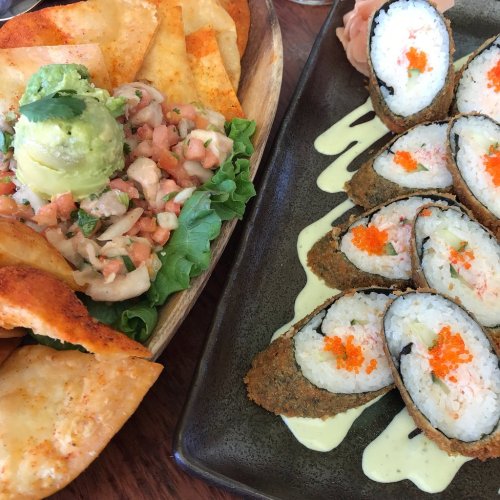 A plate featuring crispy tortilla chips, guacamole, ceviche, and sushi rolls topped with orange roe and a creamy sauce.
