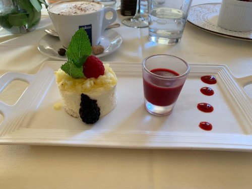 A dessert plate featuring a creamy cake topped with pineapple, berries, and a shot of raspberry sauce.