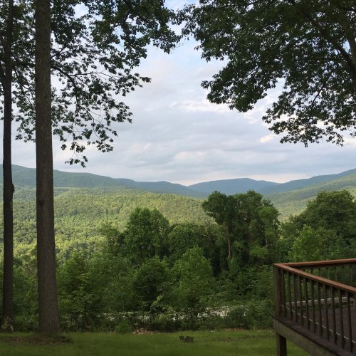A scenic view of lush green mountains and trees under a cloudy sky, with a wooden deck in the foreground.