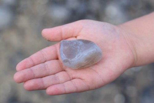A child's hand holding a smooth, translucent stone against a blurred natural background.