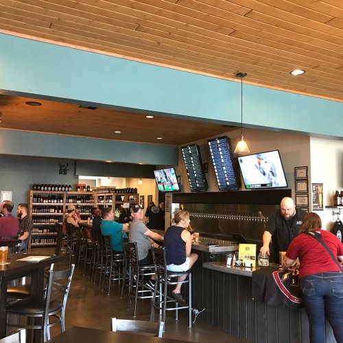 A lively bar scene with patrons seated at the counter, TVs showing sports, and shelves stocked with drinks.