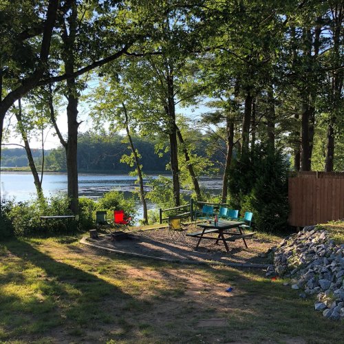 A serene lakeside scene with colorful chairs, a picnic table, and trees, reflecting a peaceful outdoor setting.