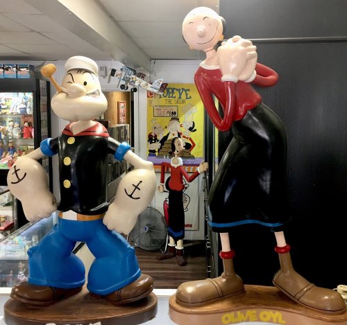 Two large cartoon statues: Popeye the Sailor with a pipe and Olive Oyl smiling, set in a colorful display area.