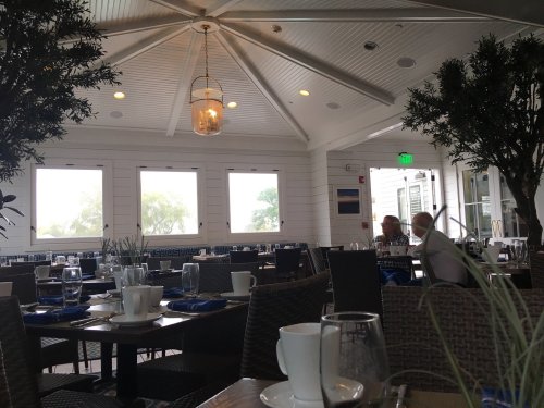 A cozy restaurant interior with tables set for dining, featuring plants and a bright, airy atmosphere.