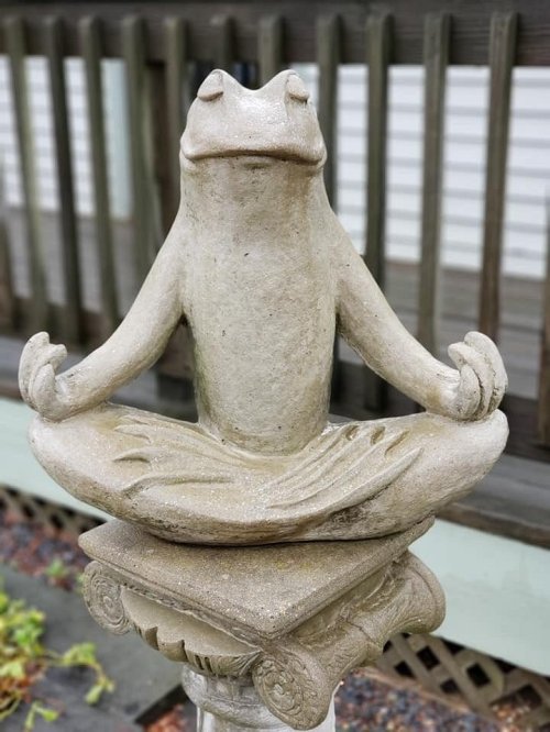 A stone frog statue in a meditative pose, sitting cross-legged on a decorative pedestal.