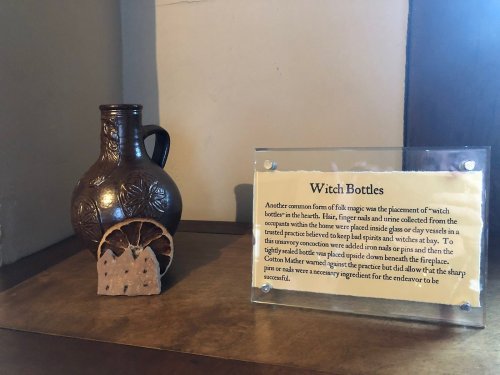 A decorative witch bottle next to an informational sign about its historical use in folk magic.