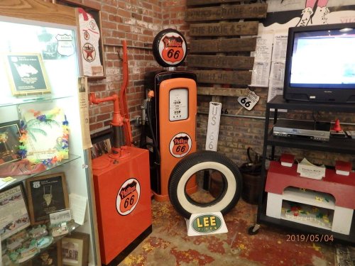 Vintage gas station display featuring a Phillips 66 pump, memorabilia, and a classic tire in a brick-walled setting.