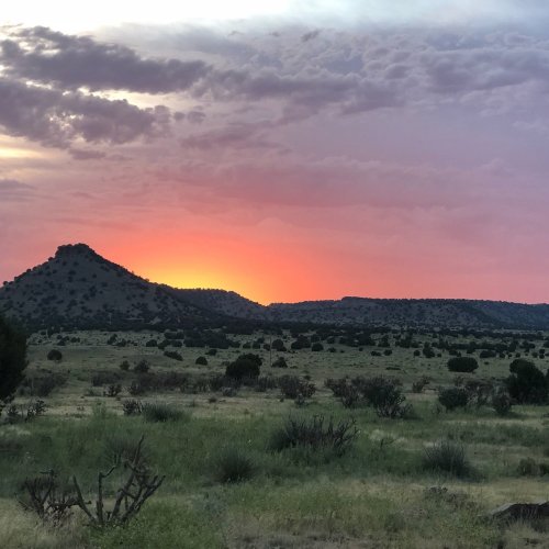 A scenic landscape at sunset, featuring rolling hills, sparse vegetation, and a colorful sky with clouds.