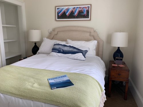 Cozy bedroom with a bed, whale pillow, bedside table, and a book titled "Nantucket" on the blanket.
