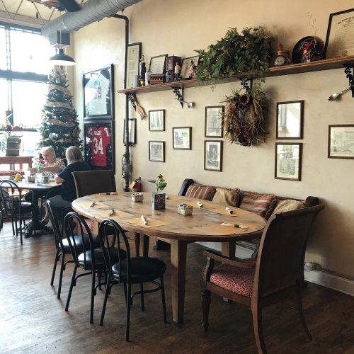 Cozy restaurant interior with a round wooden table, chairs, and festive decorations, including a Christmas tree.