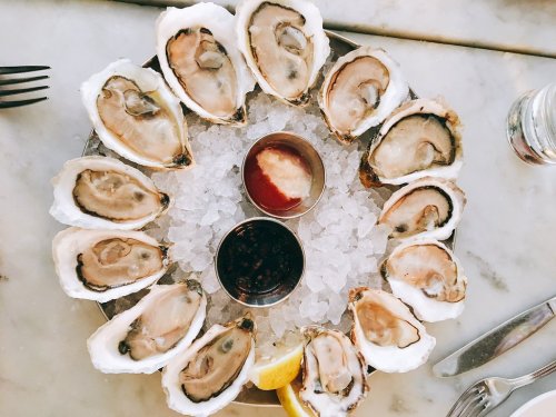 A platter of fresh oysters on ice, served with sauces and lemon wedges.