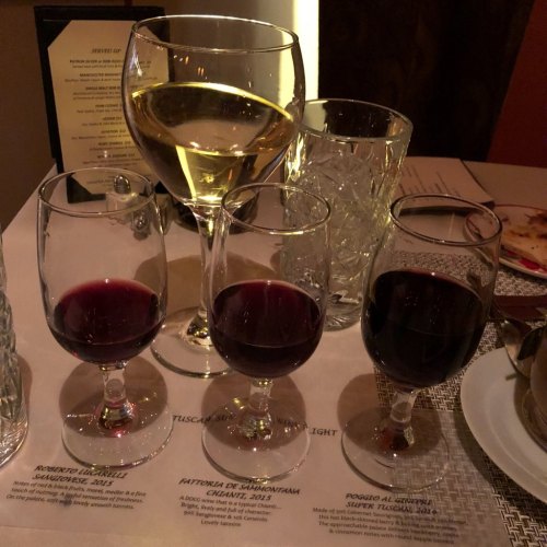 A table setting with three glasses of red wine, one glass of white wine, and a menu in a dimly lit restaurant.