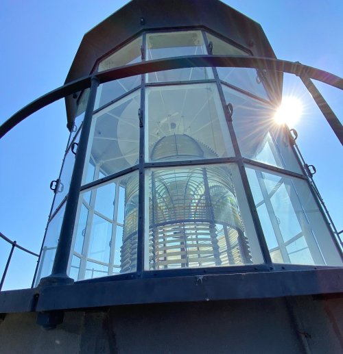 A close-up view of a lighthouse lantern room with glass panels, illuminated by sunlight.