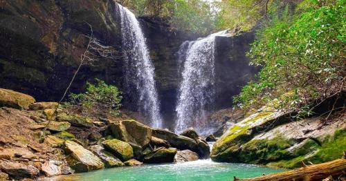 A serene waterfall cascades into a turquoise pool, surrounded by lush greenery and rocky terrain.