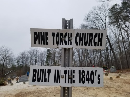 Signpost for Pine Torch Church, indicating it was built in the 1840s, surrounded by a cemetery and trees.