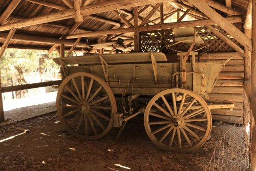 A vintage wooden wagon with large wheels, stored under a rustic wooden shelter.