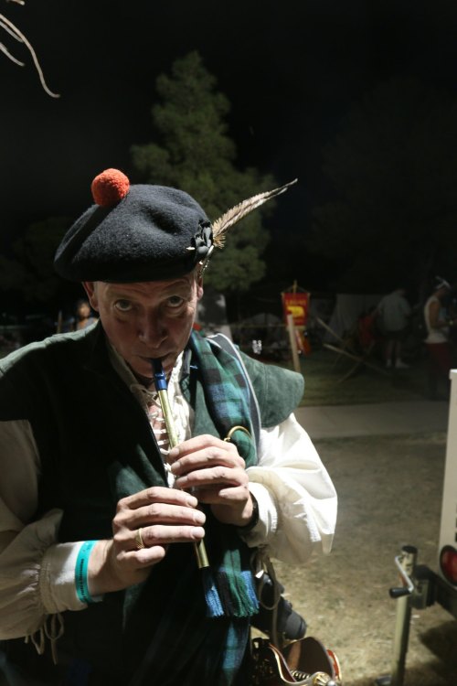 A man in a traditional outfit plays a flute at night, wearing a hat with a feather and a pom-pom.