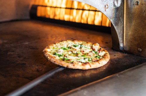 A freshly baked pizza with toppings being pulled from a wood-fired oven.