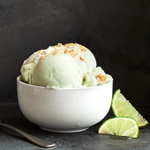 A bowl of mint ice cream topped with crumbs, accompanied by lime wedges on a dark background.