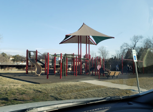 A colorful playground with a large canopy, slides, and climbing structures, set in a park on a sunny day.