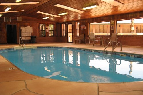Indoor swimming pool with clear blue water, wooden walls, and lounge chairs by the windows.