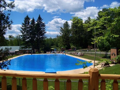 A large outdoor swimming pool surrounded by trees and lounge chairs under a blue sky with fluffy clouds.