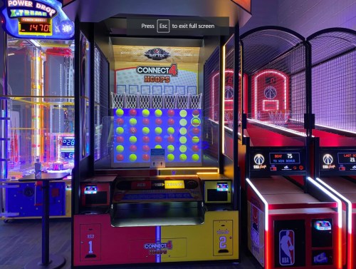 A brightly lit arcade game featuring Connect 4 and basketball hoops, with colorful balls and neon lights.