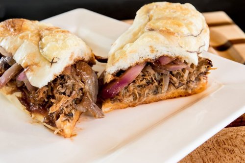 A close-up of a sandwich filled with pulled meat, onions, and sauce, served on a toasted bun.