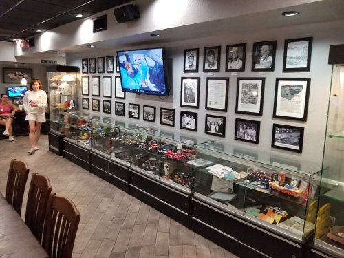 A museum display with glass cases showcasing memorabilia, framed photos on the wall, and a person walking by.