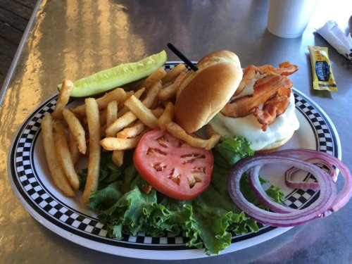 A plate with a sandwich topped with chicken, lettuce, tomato, and onion, served with fries and a pickle.