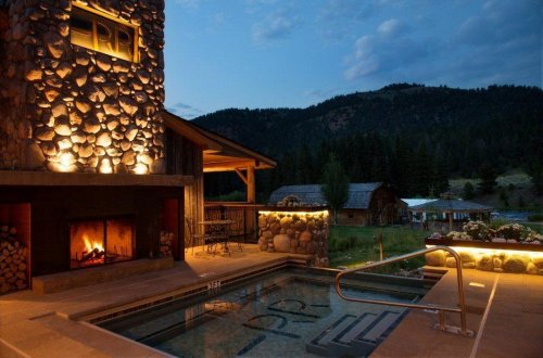 Cozy outdoor space with a stone fireplace, hot tub, and mountain views under a twilight sky.