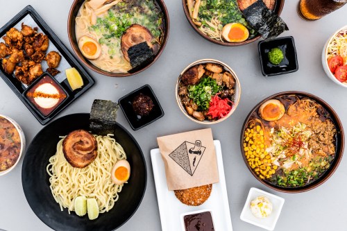 A variety of Asian dishes including ramen, fried chicken, and sides, arranged on a table with garnishes and sauces.