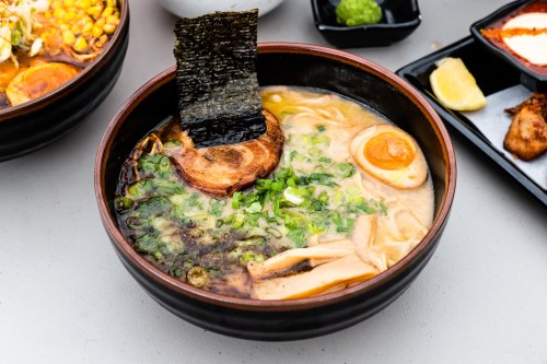 A bowl of ramen with broth, sliced pork, green onions, a soft-boiled egg, and a piece of nori on top.